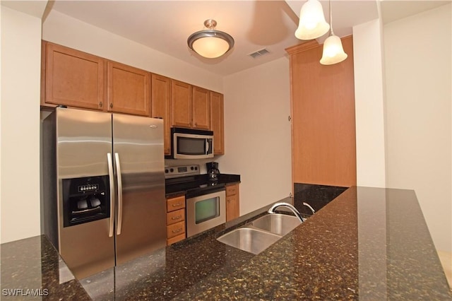 kitchen featuring pendant lighting, sink, stainless steel appliances, and dark stone counters