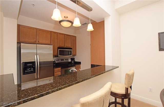 kitchen with pendant lighting, stainless steel appliances, kitchen peninsula, a kitchen bar, and dark stone counters