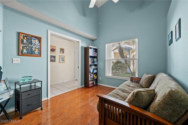 bedroom featuring ceiling fan, a high ceiling, baseboards, and wood finished floors