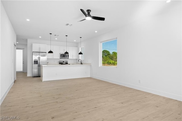 kitchen with pendant lighting, white cabinetry, sink, stainless steel appliances, and light wood-type flooring