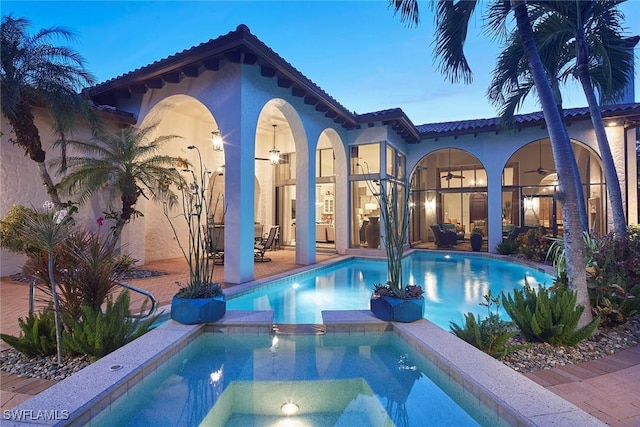 pool at dusk featuring a patio, ceiling fan, and an in ground hot tub