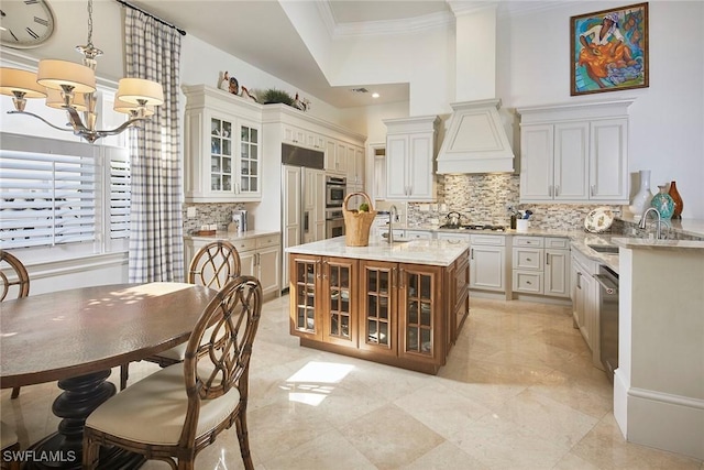 kitchen featuring premium range hood, sink, crown molding, pendant lighting, and a kitchen island with sink