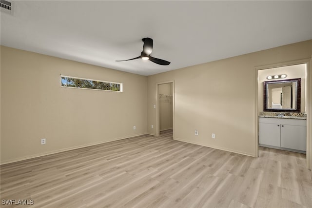 unfurnished bedroom with ensuite bathroom, a spacious closet, ceiling fan, light wood-type flooring, and a closet