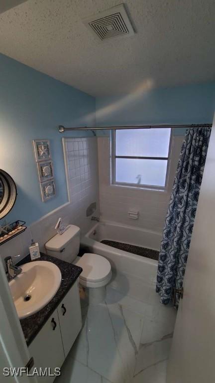 full bathroom featuring shower / tub combo with curtain, vanity, toilet, and a textured ceiling