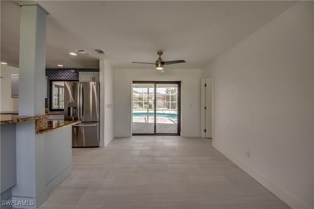 kitchen with white cabinets, ceiling fan, stainless steel fridge, and stone counters