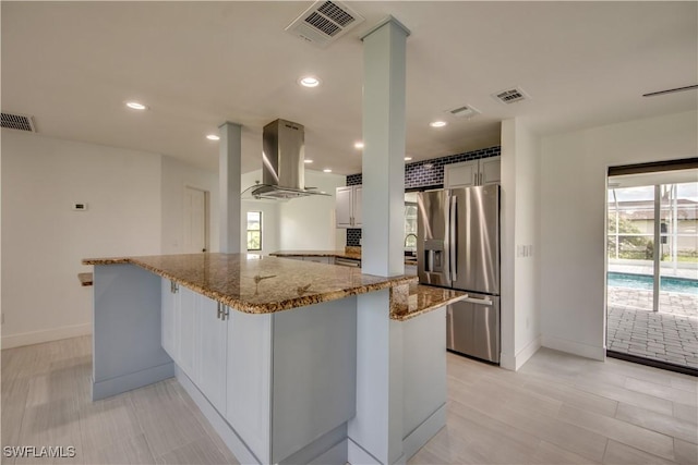 kitchen with stainless steel fridge with ice dispenser, white cabinetry, island exhaust hood, light stone counters, and kitchen peninsula