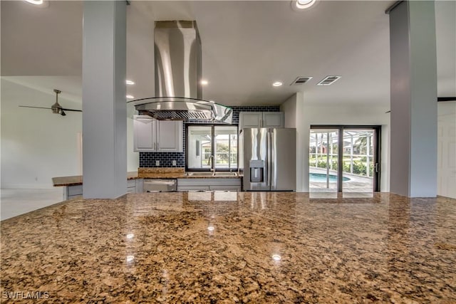 kitchen featuring sink, stone counters, stainless steel appliances, tasteful backsplash, and island exhaust hood