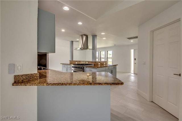 kitchen featuring high end range, kitchen peninsula, extractor fan, and dark stone countertops