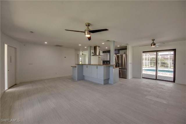 kitchen featuring stainless steel fridge with ice dispenser, wall chimney range hood, kitchen peninsula, and ceiling fan