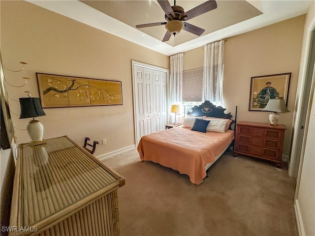 bedroom with a closet, baseboards, ceiling fan, a raised ceiling, and carpet flooring