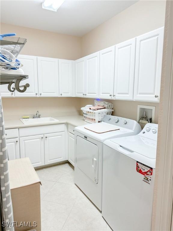 laundry room with sink, washing machine and dryer, cabinets, and light tile patterned flooring