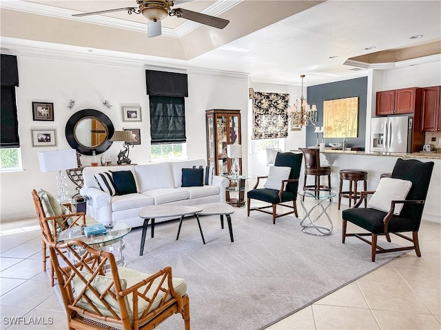 living room with ornamental molding, a raised ceiling, ceiling fan with notable chandelier, and light tile patterned floors