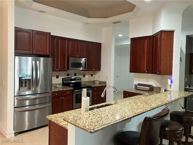 kitchen with sink, stainless steel appliances, light stone counters, a kitchen bar, and kitchen peninsula