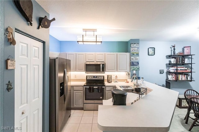 kitchen featuring appliances with stainless steel finishes, decorative light fixtures, sink, light tile patterned floors, and kitchen peninsula