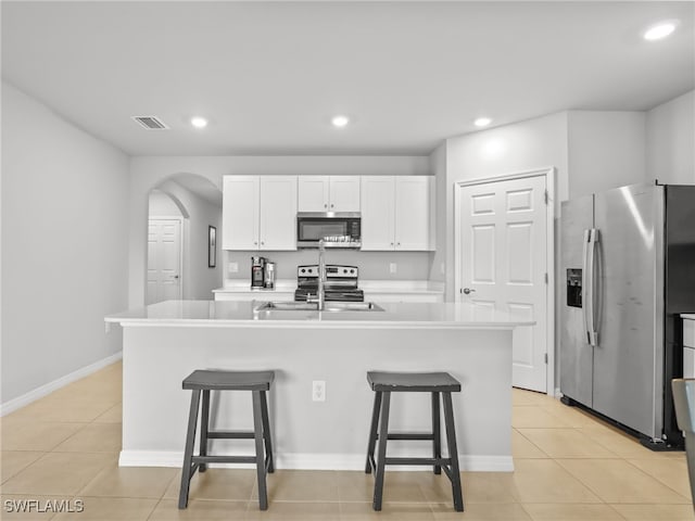 kitchen featuring light tile patterned flooring, a breakfast bar, white cabinetry, a center island with sink, and stainless steel appliances