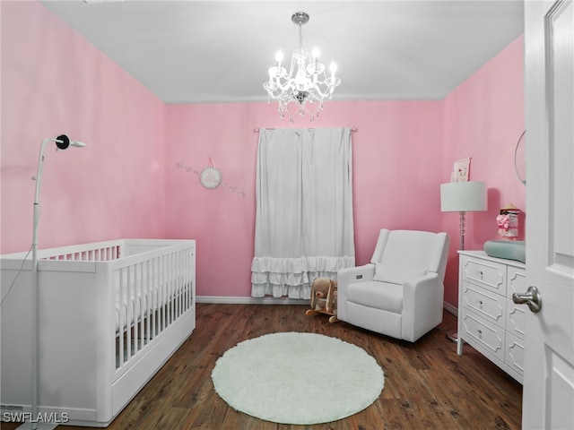 bedroom with a nursery area, dark wood-type flooring, and an inviting chandelier