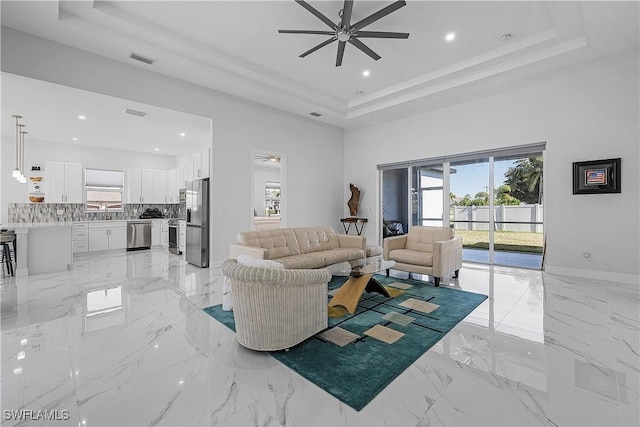 living area featuring plenty of natural light, ceiling fan, visible vents, and a raised ceiling