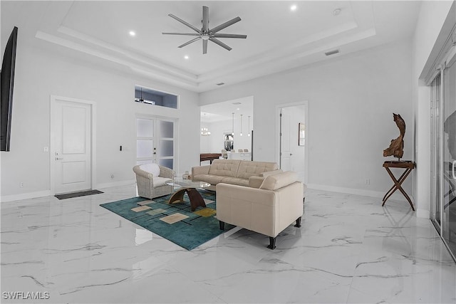 living area with ceiling fan with notable chandelier, a high ceiling, visible vents, baseboards, and a raised ceiling