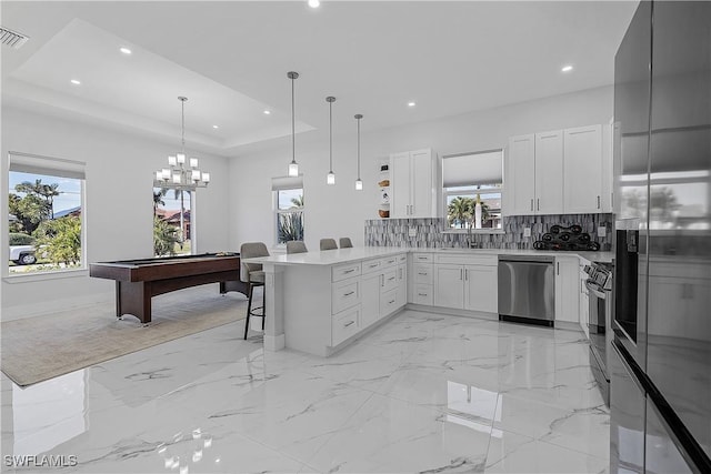 kitchen with decorative backsplash, a raised ceiling, a peninsula, stainless steel appliances, and a kitchen bar