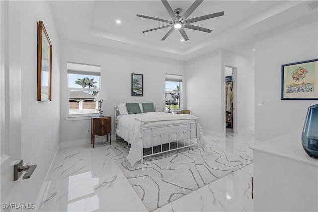 bedroom featuring recessed lighting, baseboards, marble finish floor, a tray ceiling, and a walk in closet