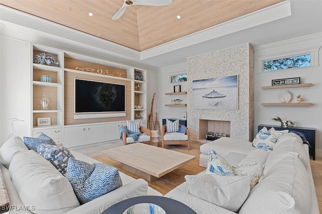 living room with built in shelves, ornamental molding, a fireplace, and a raised ceiling