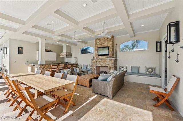 dining space featuring ceiling fan, a stone fireplace, coffered ceiling, and beam ceiling