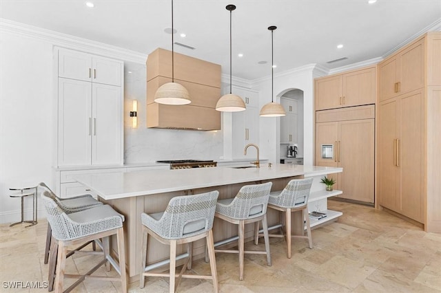 kitchen with light brown cabinetry, decorative light fixtures, sink, a large island with sink, and paneled built in fridge