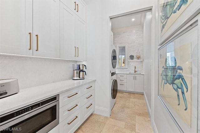 kitchen with white cabinetry, stacked washing maching and dryer, sink, and backsplash