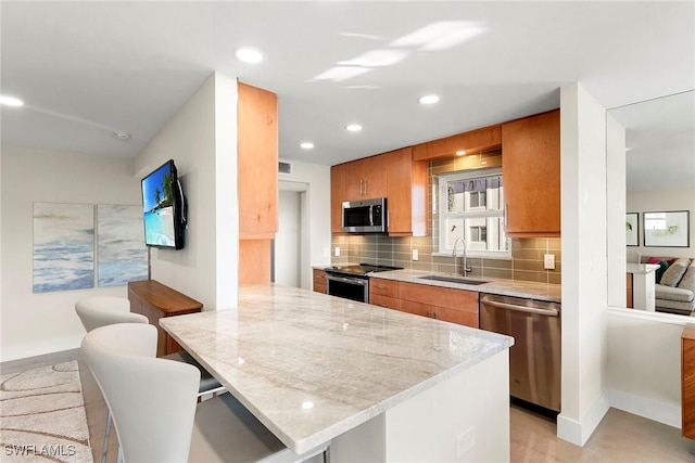 kitchen with appliances with stainless steel finishes, sink, a kitchen bar, decorative backsplash, and light stone countertops