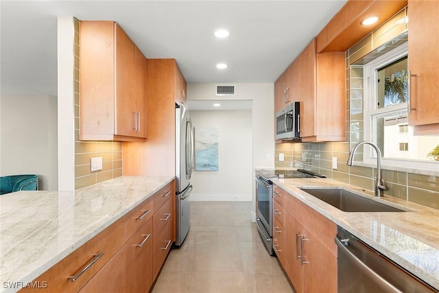 kitchen with light stone counters, sink, decorative backsplash, and stainless steel appliances