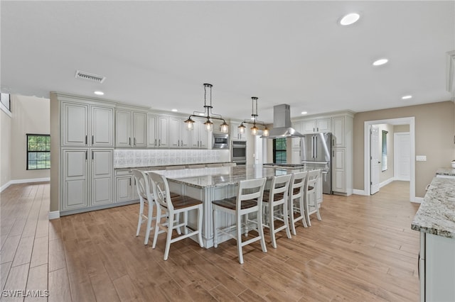 kitchen featuring hanging light fixtures, stainless steel appliances, a spacious island, island range hood, and light stone countertops