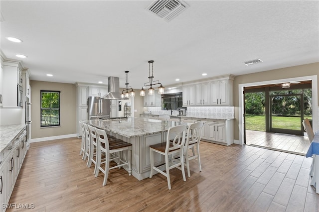 kitchen with a spacious island, hanging light fixtures, island exhaust hood, stainless steel appliances, and decorative backsplash