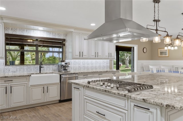 kitchen featuring decorative light fixtures, sink, island exhaust hood, light stone counters, and stainless steel appliances