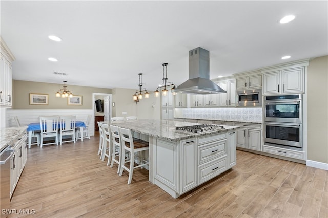 kitchen featuring pendant lighting, island range hood, a center island, stainless steel appliances, and light stone countertops