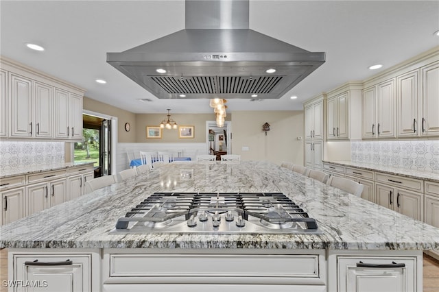 kitchen with light stone counters, island range hood, stainless steel gas stovetop, and a breakfast bar area