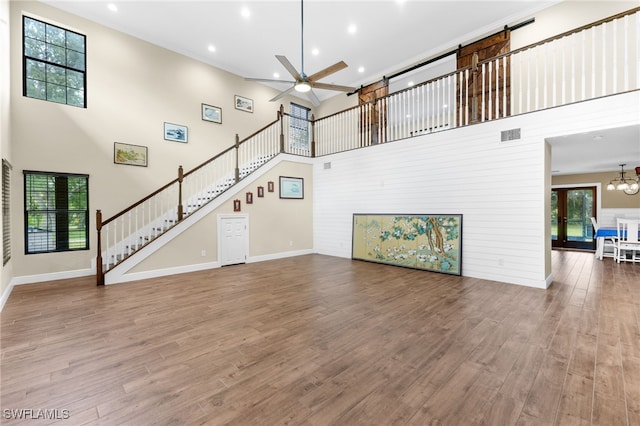 unfurnished living room with hardwood / wood-style flooring, ceiling fan with notable chandelier, and a high ceiling