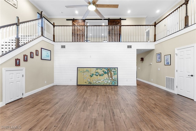 unfurnished living room with ceiling fan, ornamental molding, hardwood / wood-style floors, and a high ceiling