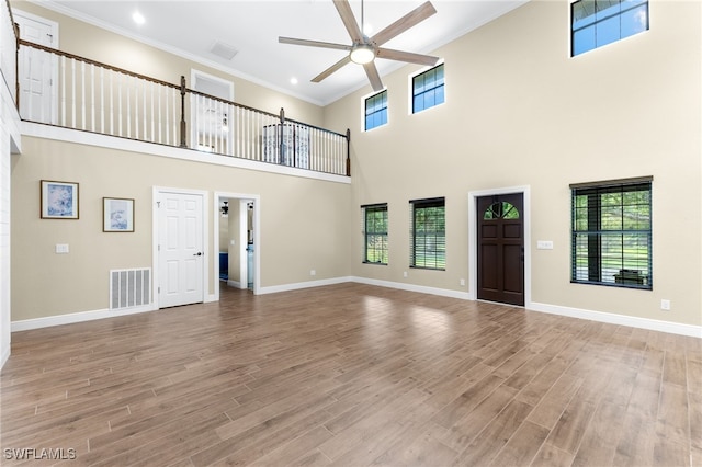 unfurnished living room featuring ornamental molding, a towering ceiling, ceiling fan, and light hardwood / wood-style flooring