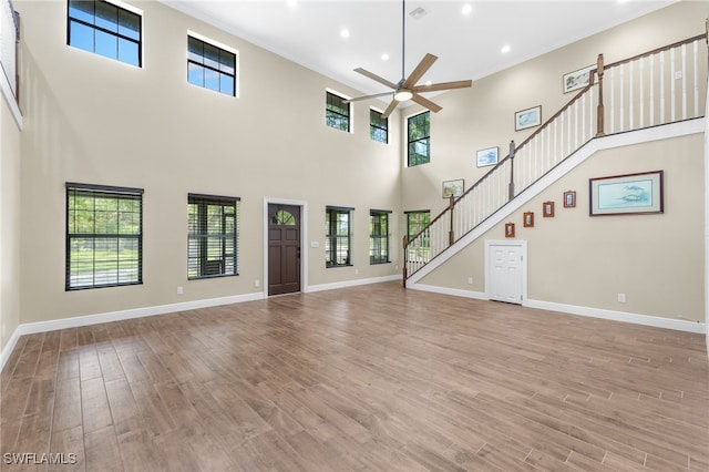 unfurnished living room featuring a towering ceiling, light hardwood / wood-style floors, and ceiling fan