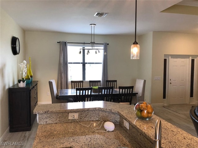 kitchen with light stone counters, hanging light fixtures, and light hardwood / wood-style flooring