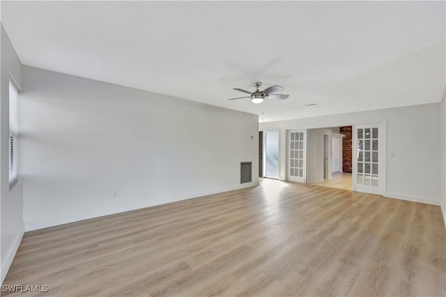 empty room with ceiling fan, a brick fireplace, light wood-type flooring, and french doors