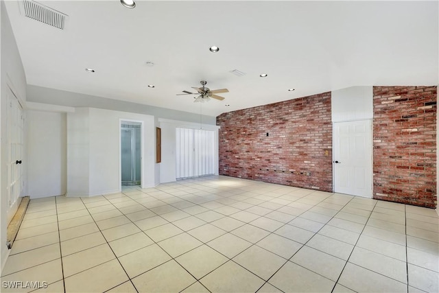 spare room featuring light tile patterned floors, ceiling fan, and brick wall