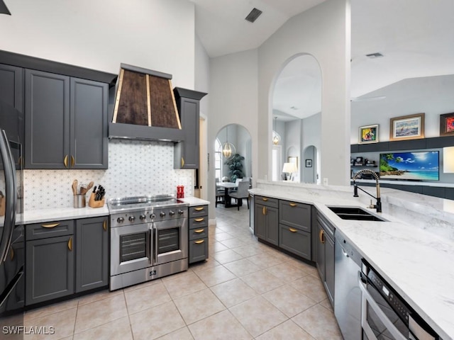 kitchen featuring vaulted ceiling, gray cabinetry, decorative backsplash, custom exhaust hood, and stainless steel range