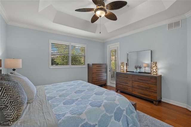 bedroom featuring hardwood / wood-style flooring, ornamental molding, ceiling fan, and a tray ceiling