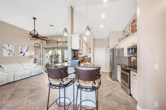 kitchen featuring appliances with stainless steel finishes, a breakfast bar, tasteful backsplash, white cabinets, and dark stone counters