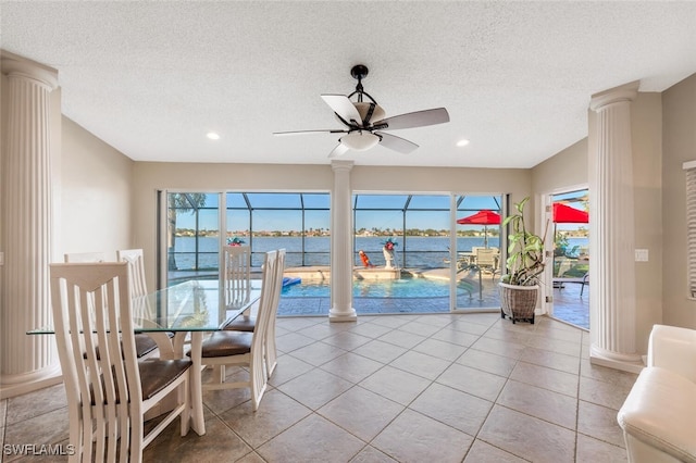 tiled dining area with ornate columns, a water view, a textured ceiling, and ceiling fan