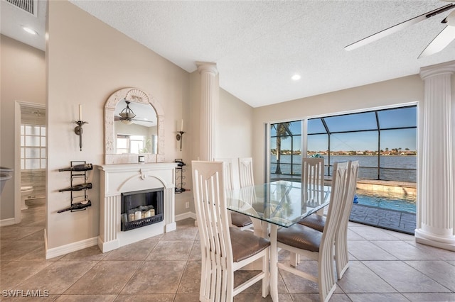 dining area featuring a water view, light tile patterned floors, a textured ceiling, and ornate columns