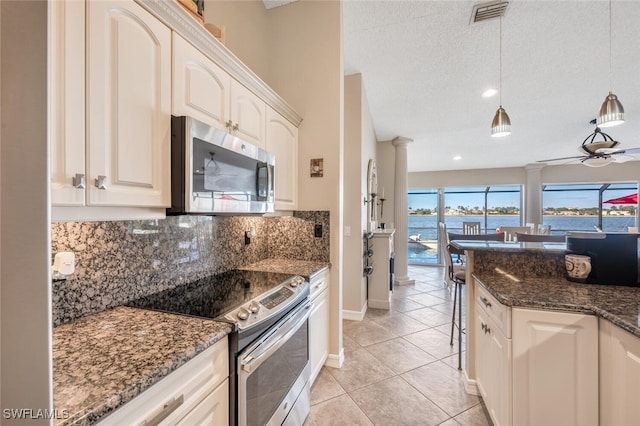 kitchen featuring a water view, decorative light fixtures, light tile patterned floors, appliances with stainless steel finishes, and dark stone counters