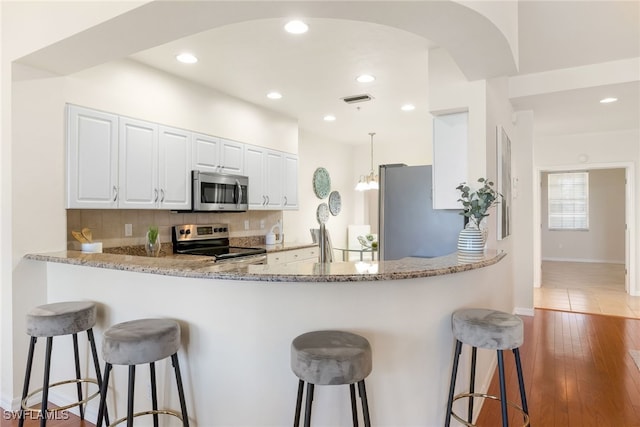 kitchen featuring white cabinetry, a breakfast bar area, backsplash, light stone counters, and stainless steel appliances