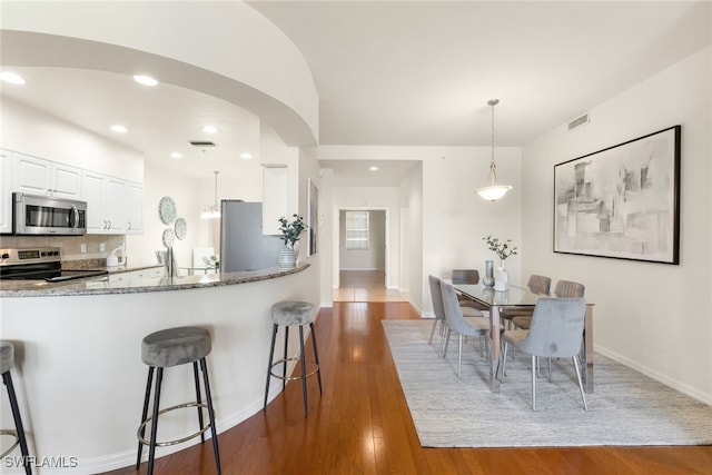 kitchen featuring stone countertops, appliances with stainless steel finishes, dark hardwood / wood-style floors, pendant lighting, and white cabinets